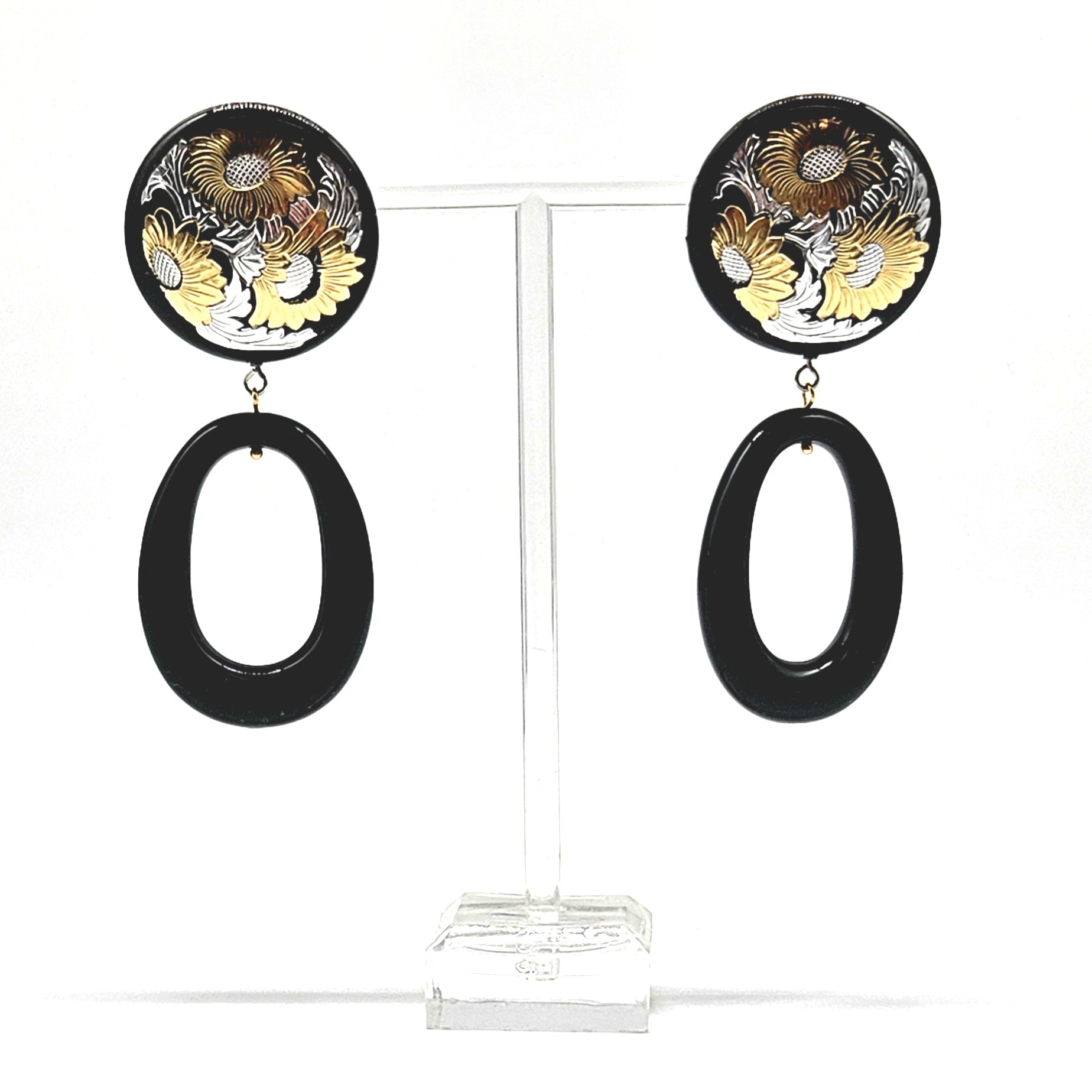 Pair of earrings with floral design and black oval shapes on a clear stand.