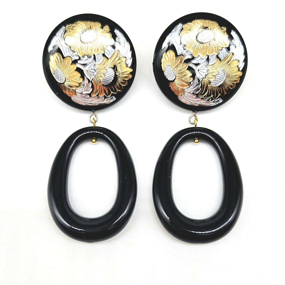Pair of earrings with black oval drops and floral designs in gold and silver on a white background