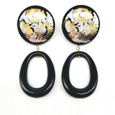 Pair of earrings with black oval drops and floral designs in gold and silver on a white background