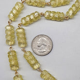 Necklace with yellow beads next to a U.S. quarter for size comparison on a light gray background