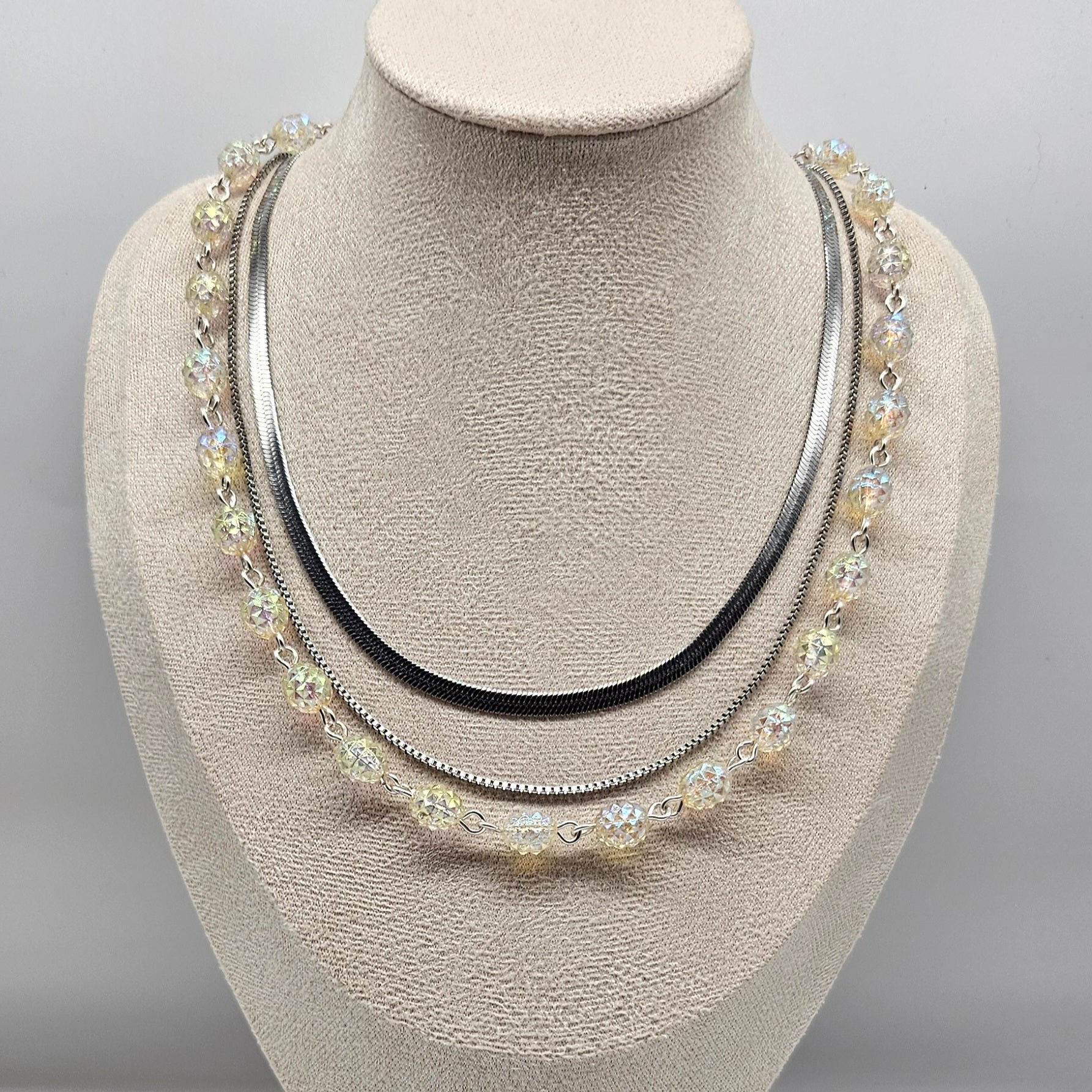 Silver necklace with multiple strands on a mannequin bust against a gray background