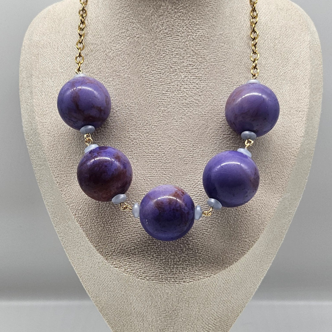 Necklace with purple beads on a gray stand
