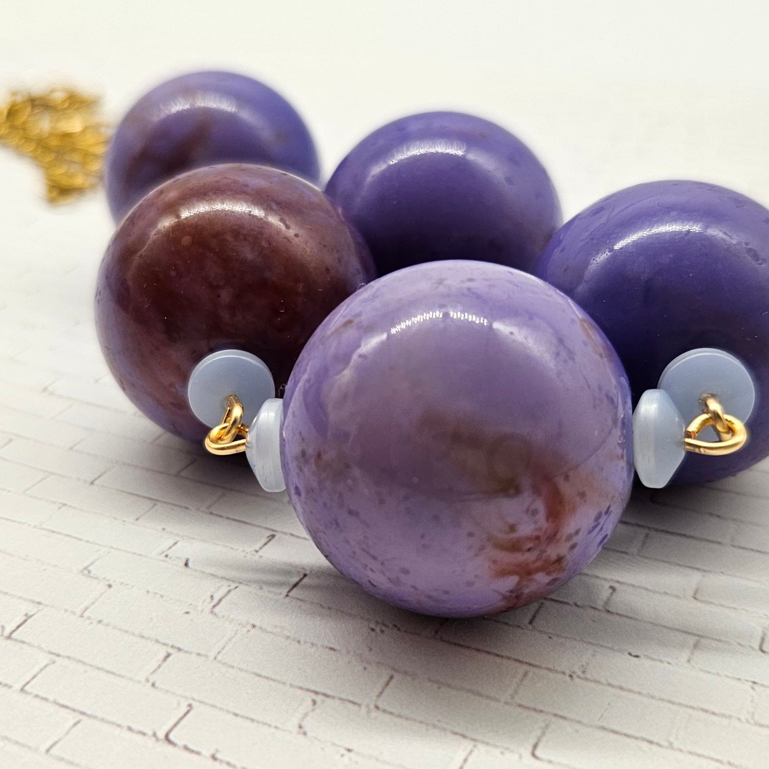 Close-up of a necklace with purple and brown marbled beads on a textured surface