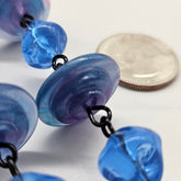 Close-up of blue and purple beads with a coin for scale on a white background