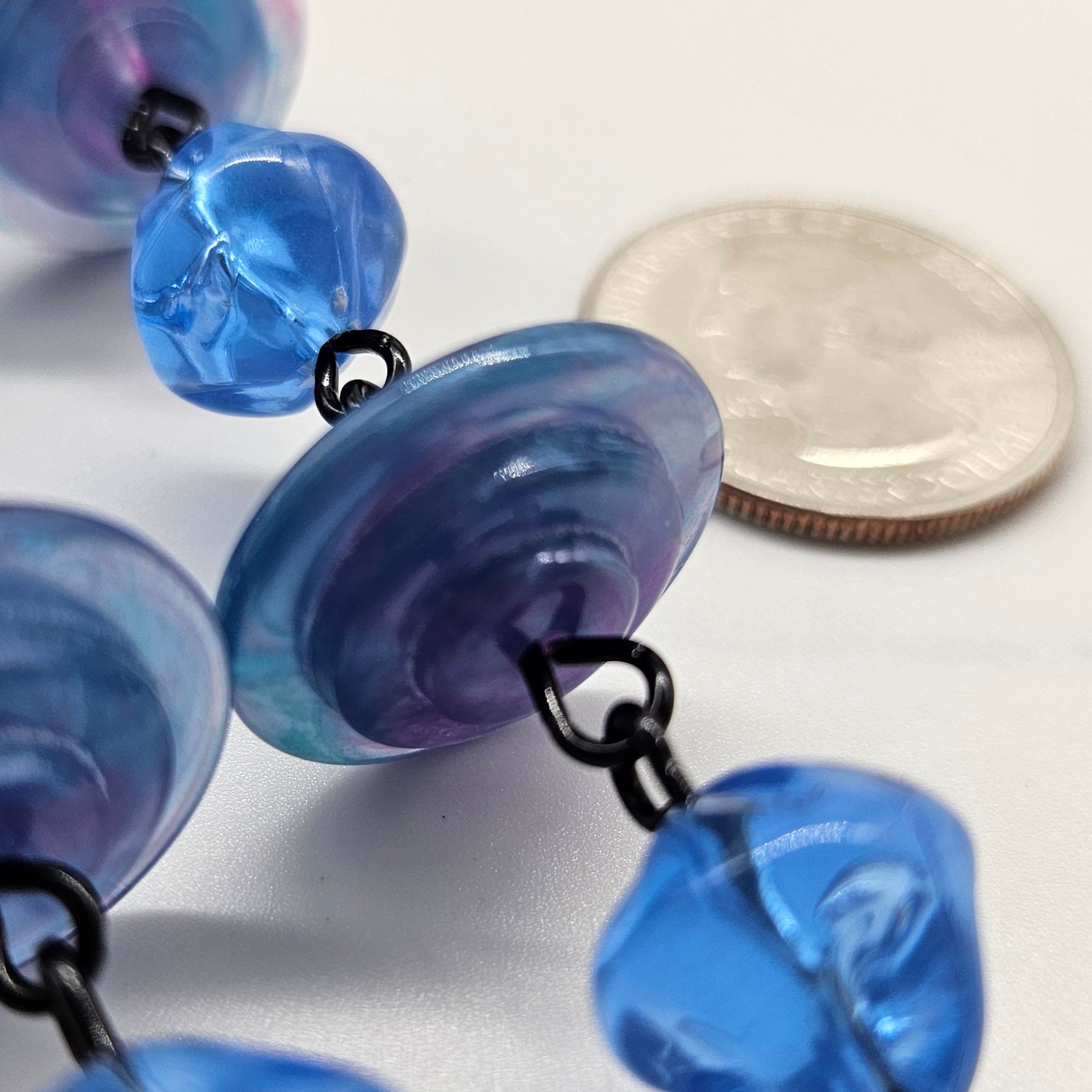 Close-up of blue and purple beads with a coin for scale on a white background