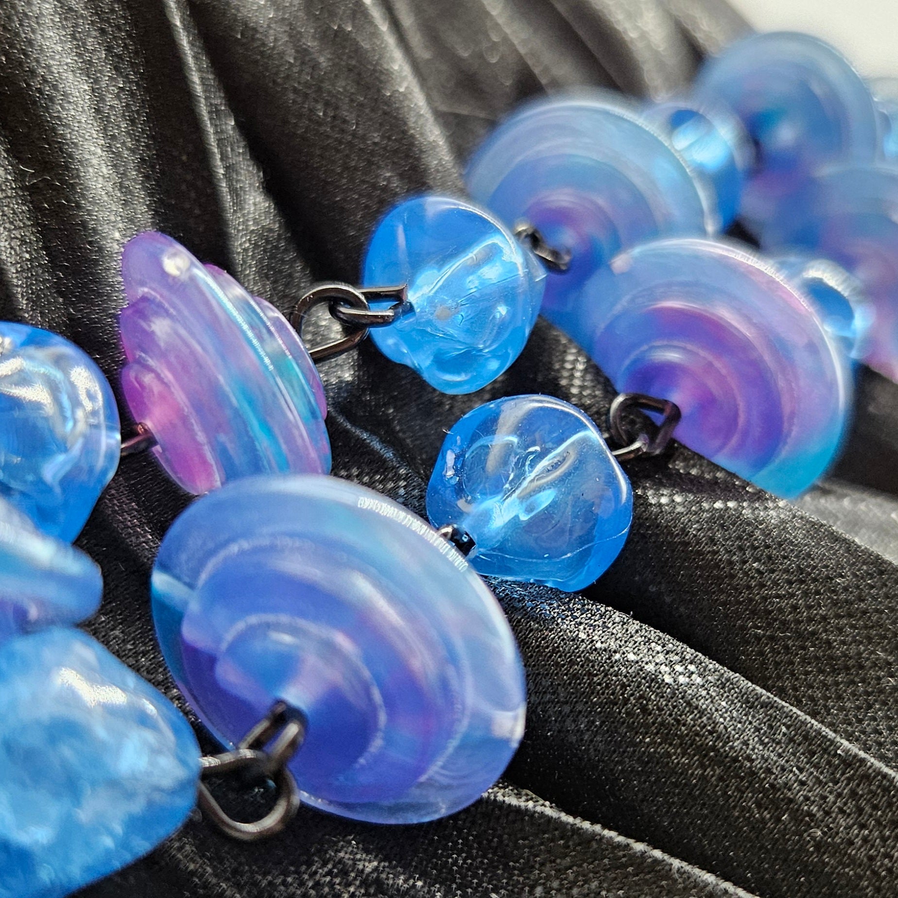 Necklace with blue and purple marbled beads on a black fabric background