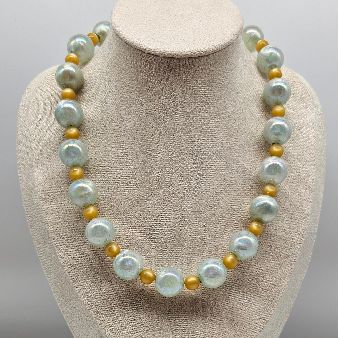 Pearlized lucite and golden bead necklace on a mannequin bust against a neutral background