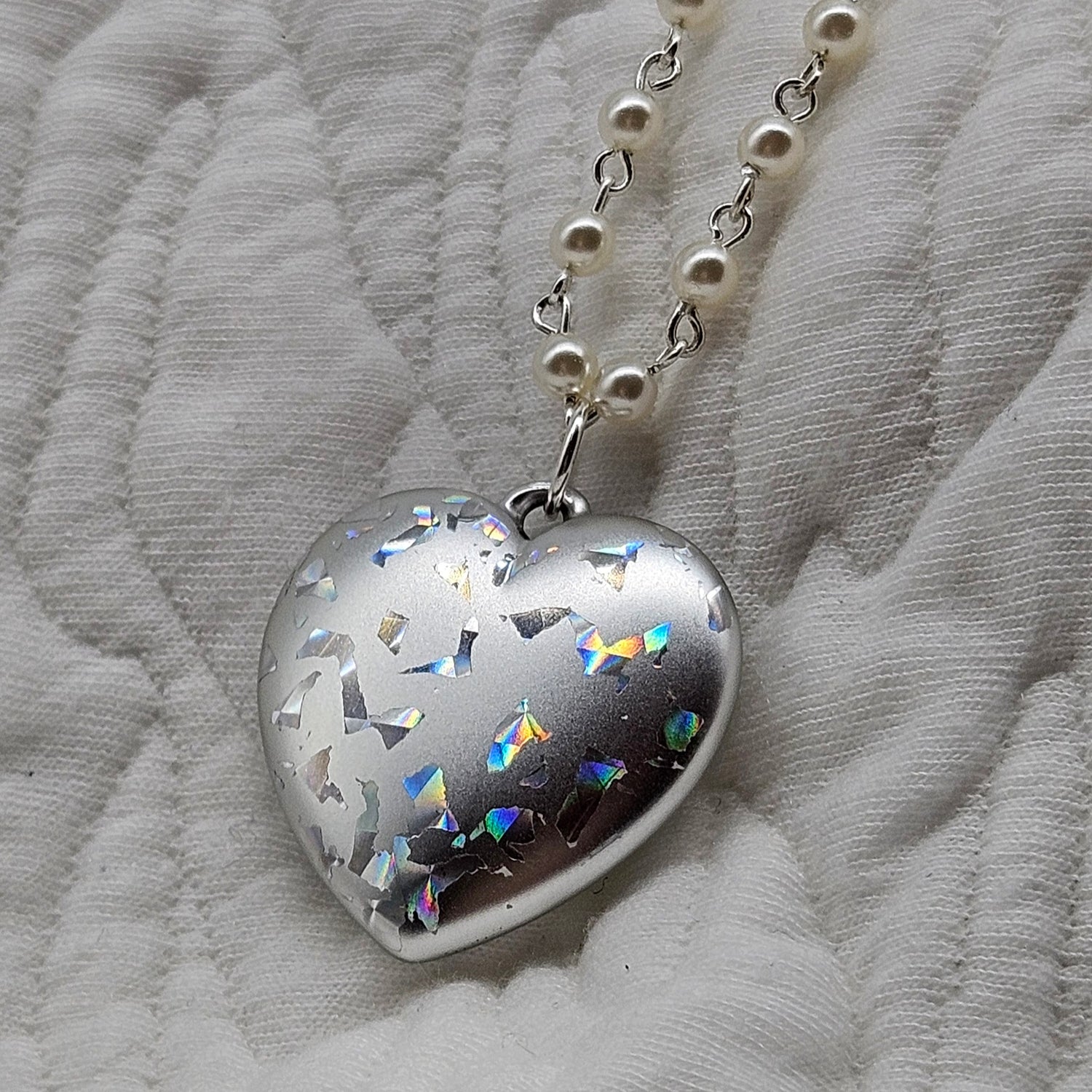 Heart-shaped silver pendant with colorful accents on a white fabric background