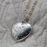 Heart-shaped silver pendant with colorful accents on a white fabric background