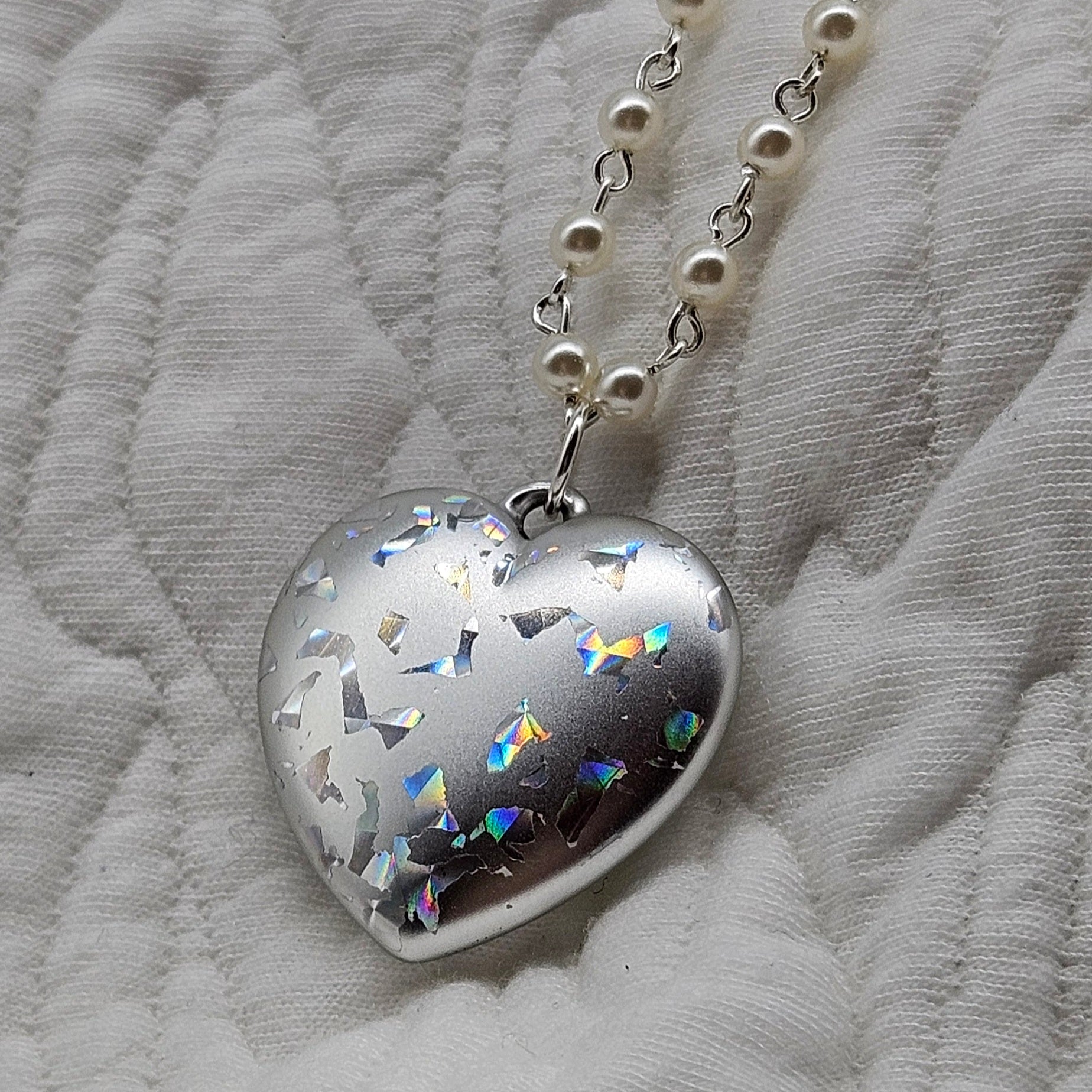 Heart-shaped silver pendant with colorful accents on a white fabric background