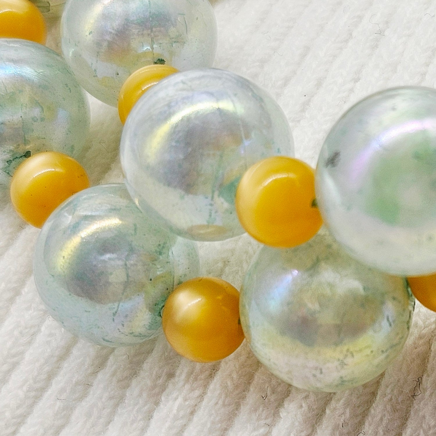 Close-up of a necklace with large pearlized beads and smaller golden yellow spacers on a textured white background