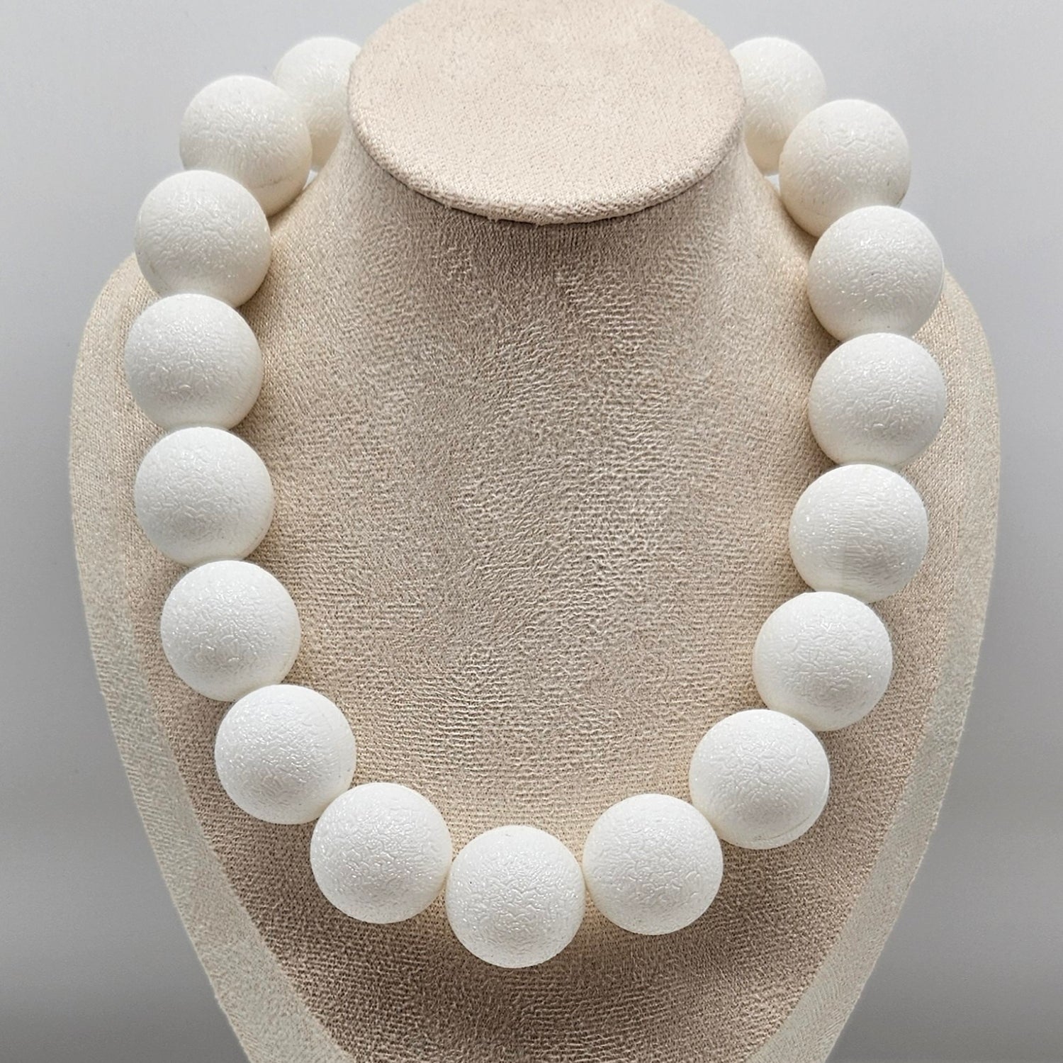 White spherical necklace on a beige mannequin bust against a gray background
