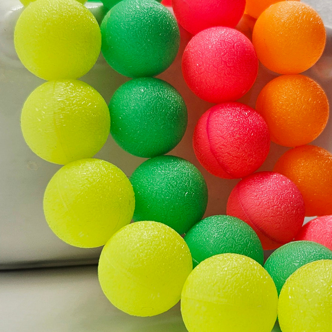 Close-up of colorful lucite beads in neon yellow, green, pink, and orange on a white surface.