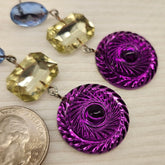 Purple and yellow earrings on a light wooden surface with a quarter for scale.