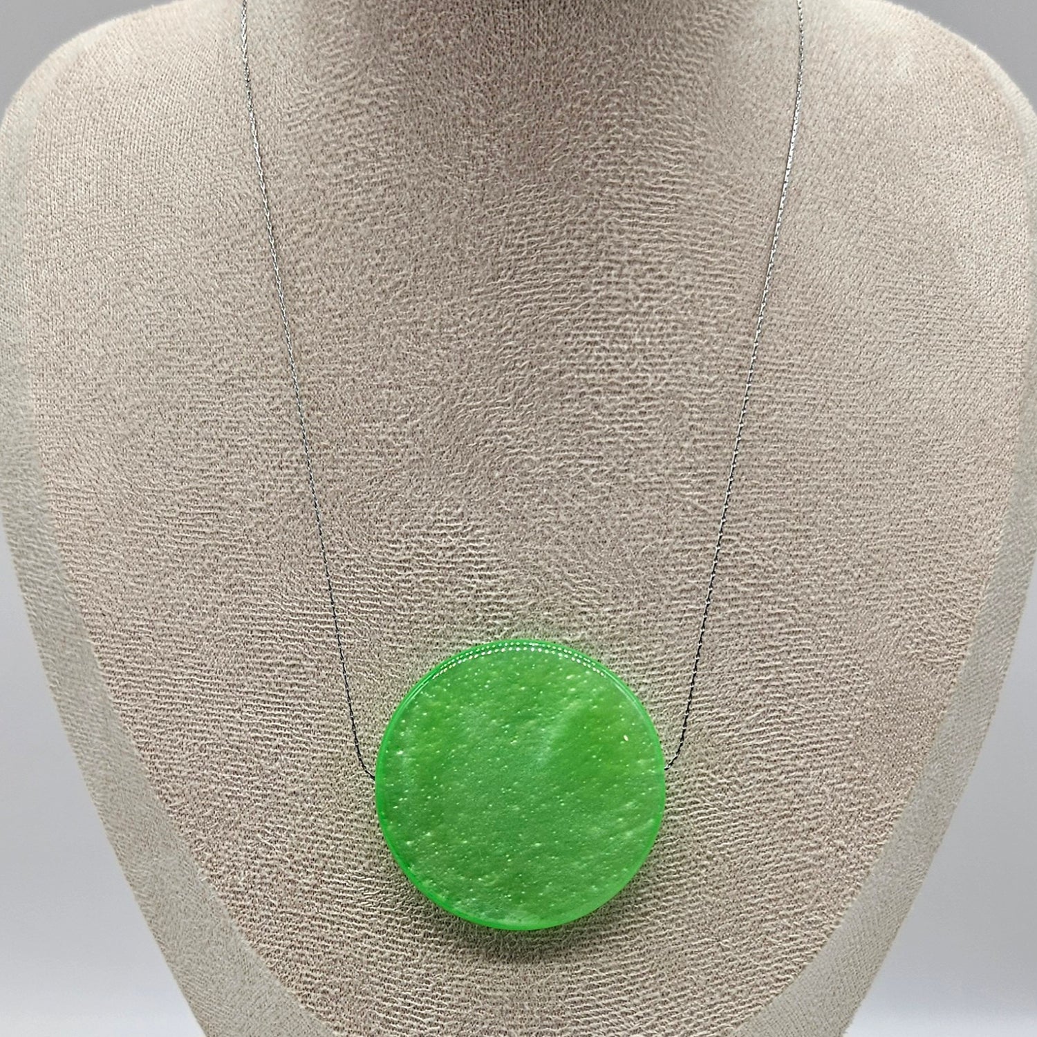 Green circular pendant on a gray fabric background