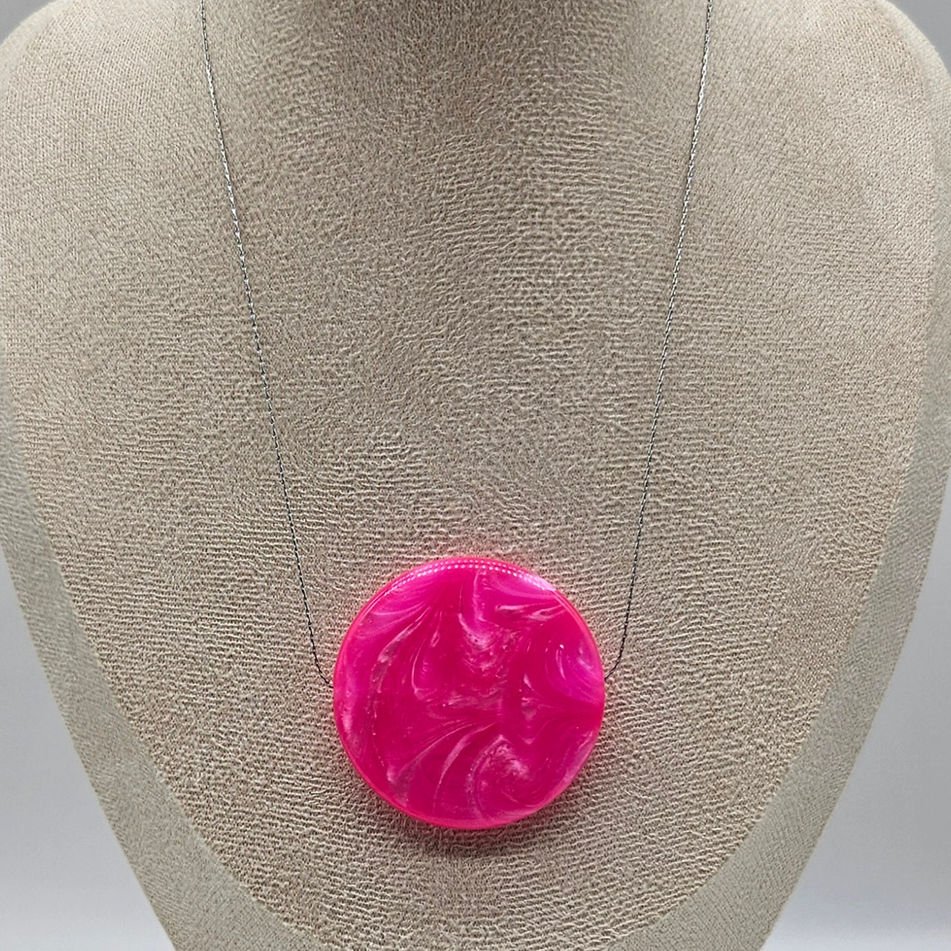 Pink circular brooch on a gray jewelry display