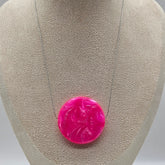 Pink circular brooch on a gray jewelry display