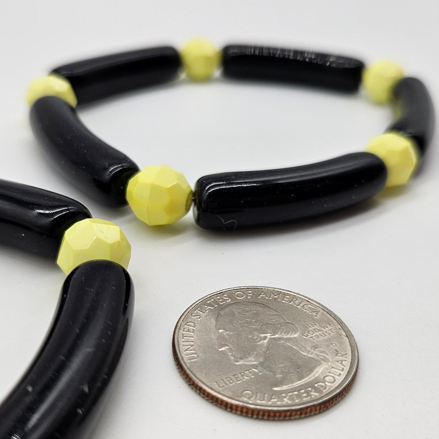 Black and yellow beaded brcelet next to a quarter for size reference on a white background