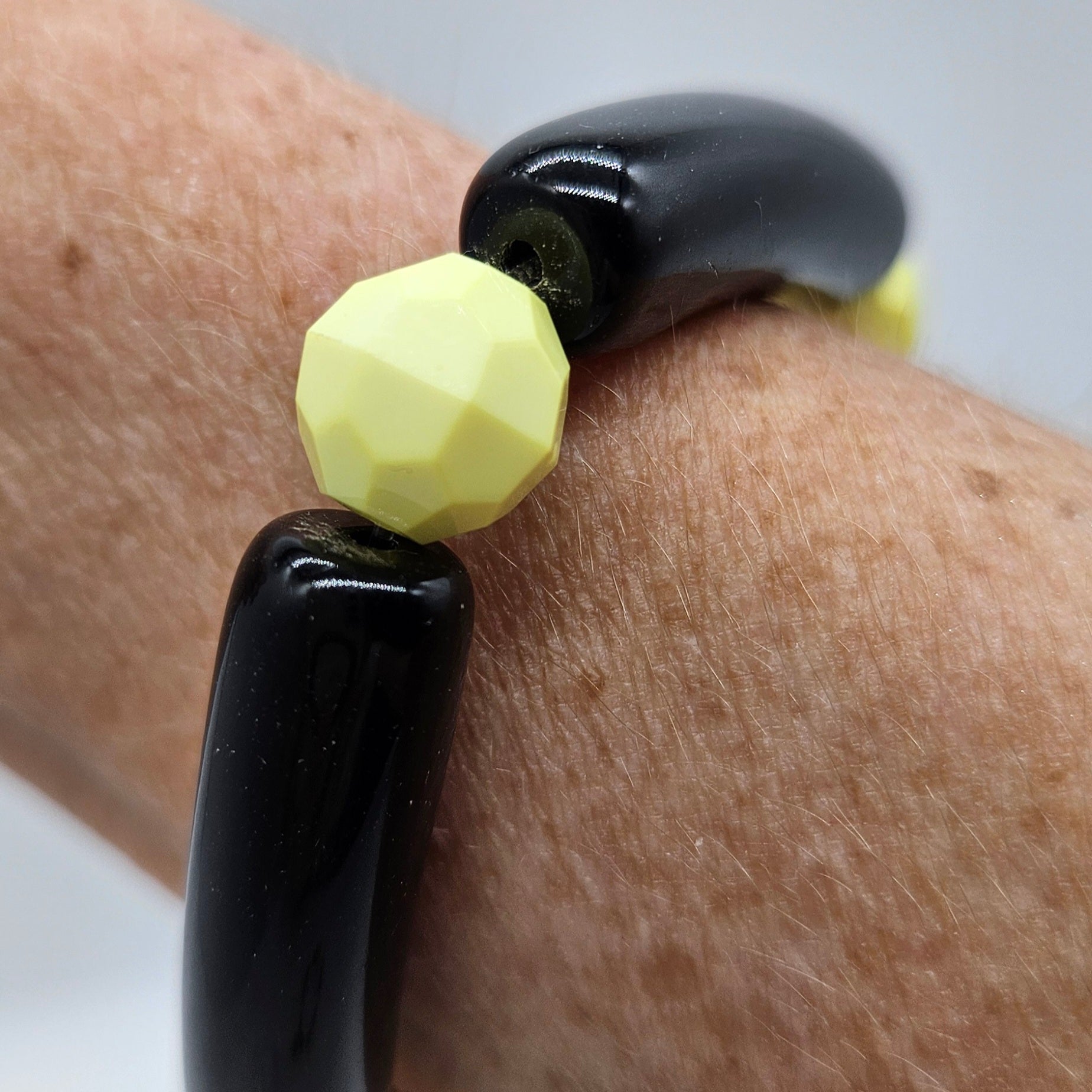 Close-up of a black and yellow bracelet on a wrist with a neutral background