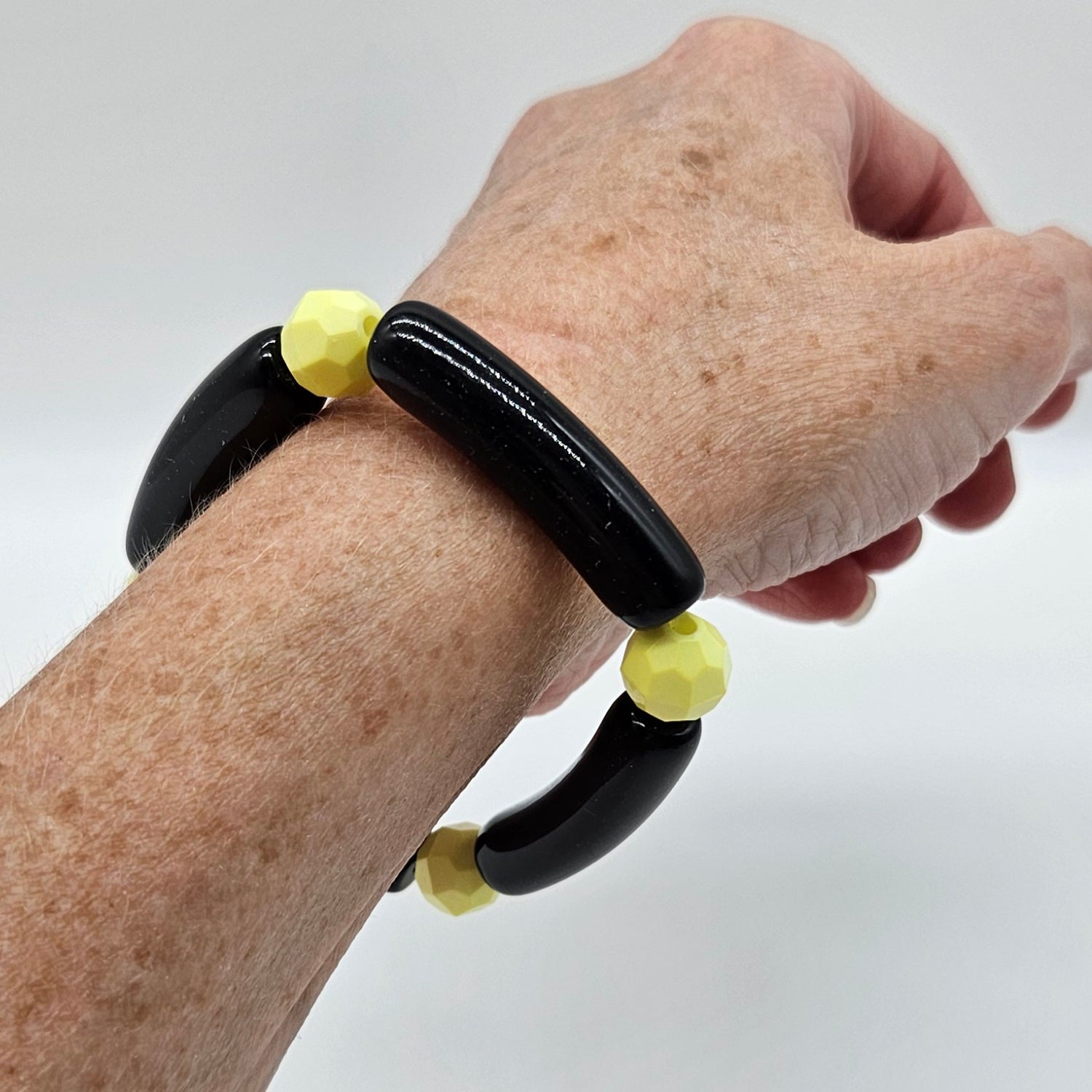 Hand wearing a black and yellow beaded bracelet on a plain background