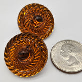 Two ornate orange lucite earrings next to a U.S. quarter coin on a white background