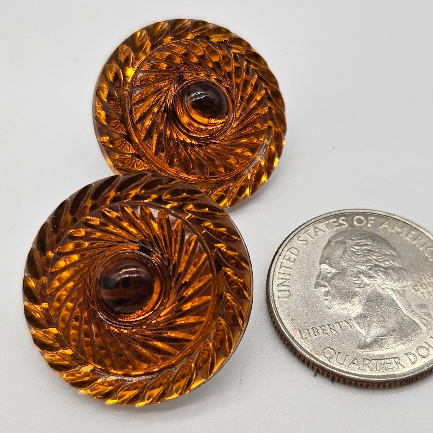 Two ornate orange lucite earrings next to a U.S. quarter coin on a white background