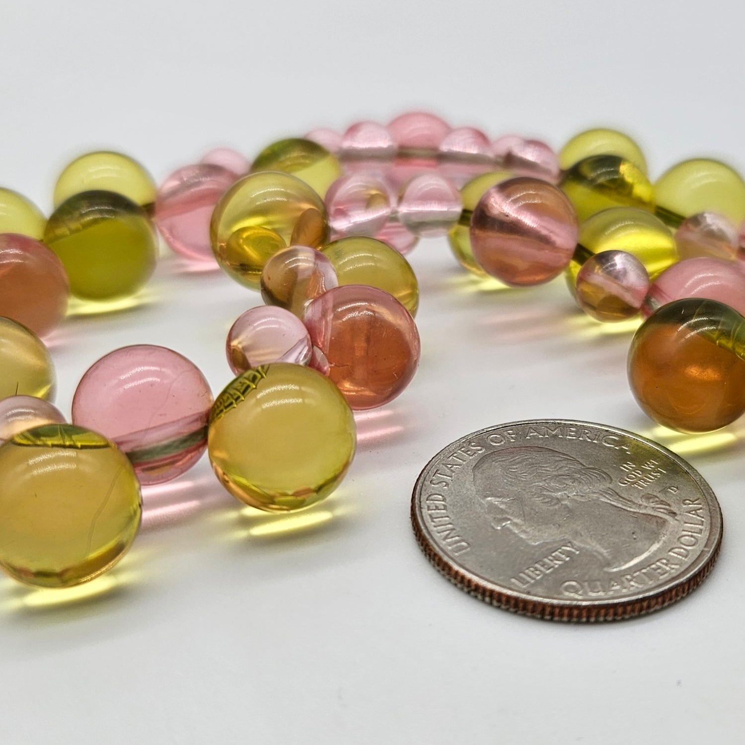 Colorful lucite beads with a quarter for scale on a white background