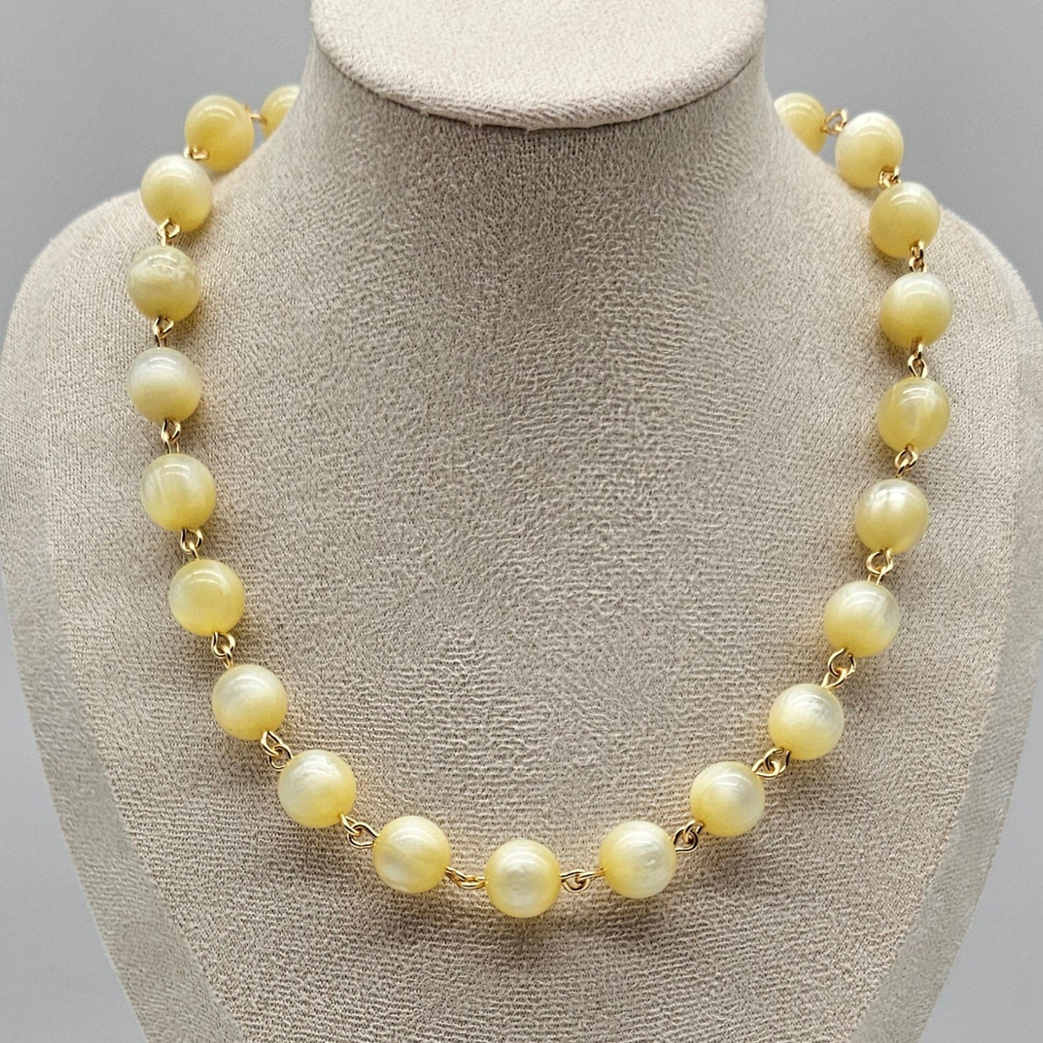 Cream colored moonglow beaded  necklace on a mannequin bust with a gray background
