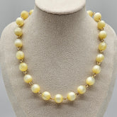 Cream colored moonglow beaded  necklace on a mannequin bust with a gray background