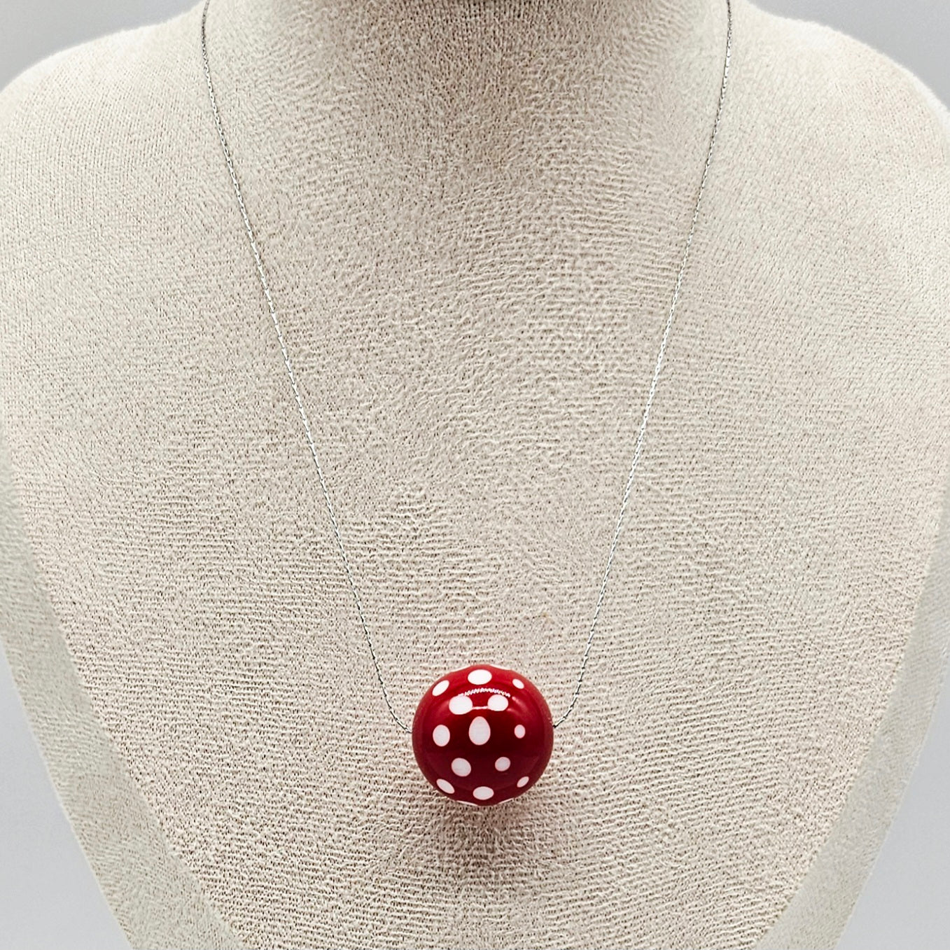 Red polka dot pendant on a necklace displayed on a mannequin bust.