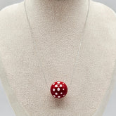 Red polka dot pendant on a necklace displayed on a mannequin bust.