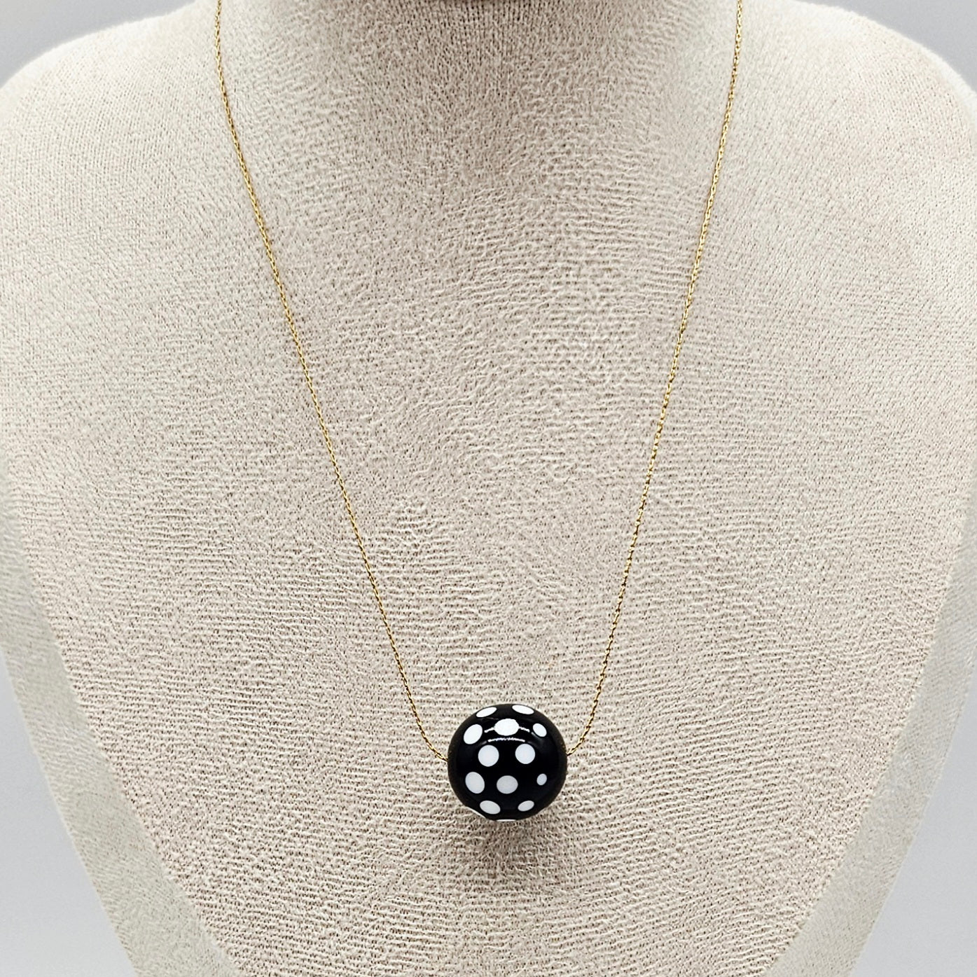 Necklace with a black pendant featuring white polka dots on a mannequin bust.