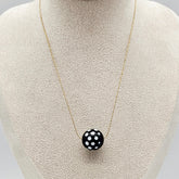 Necklace with a black pendant featuring white polka dots on a mannequin bust.