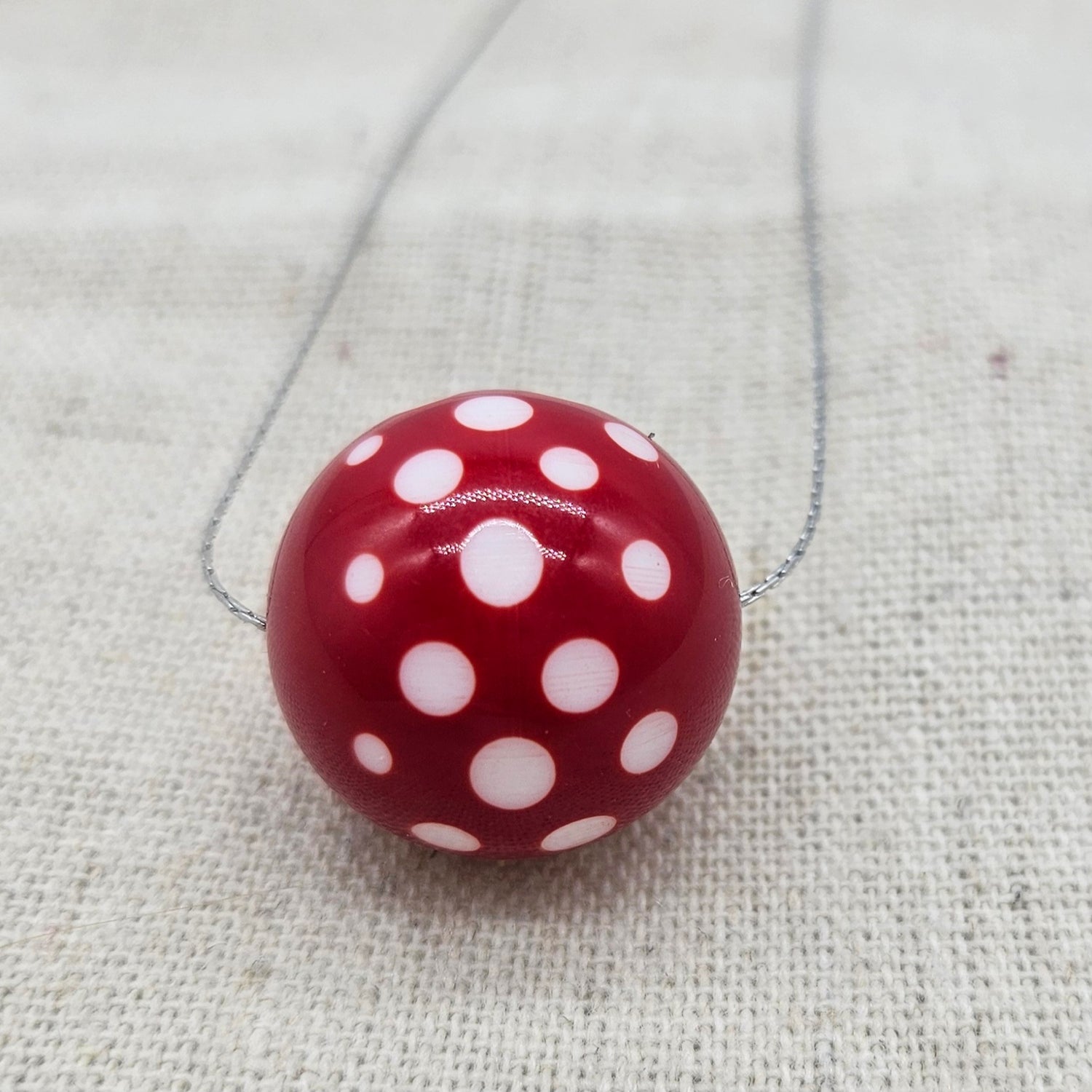 Red round pendant with white polka dots on a chain against a textured beige background