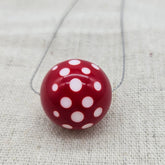 Red round pendant with white polka dots on a chain against a textured beige background