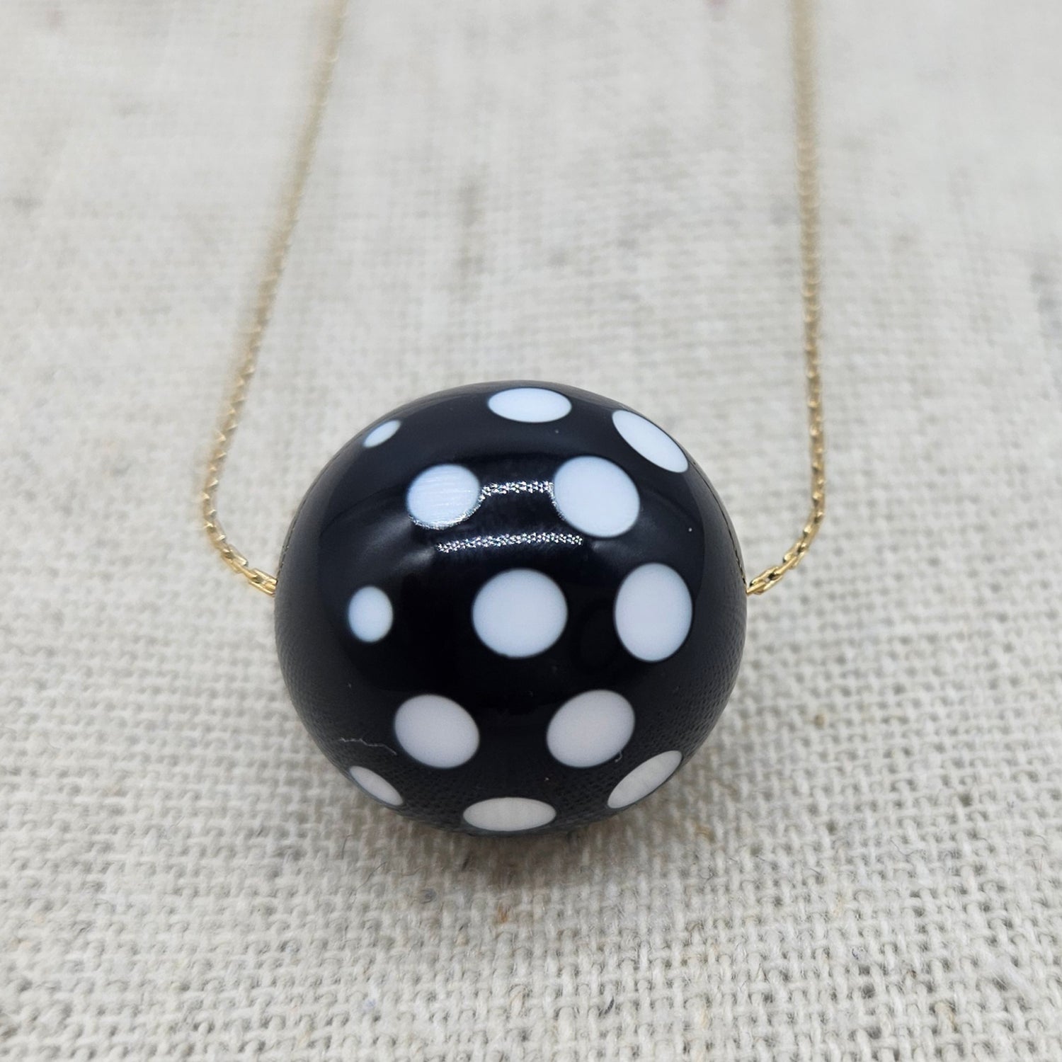 Black necklace with white polka dots on a textured beige background