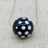 Black necklace with white polka dots on a textured beige background