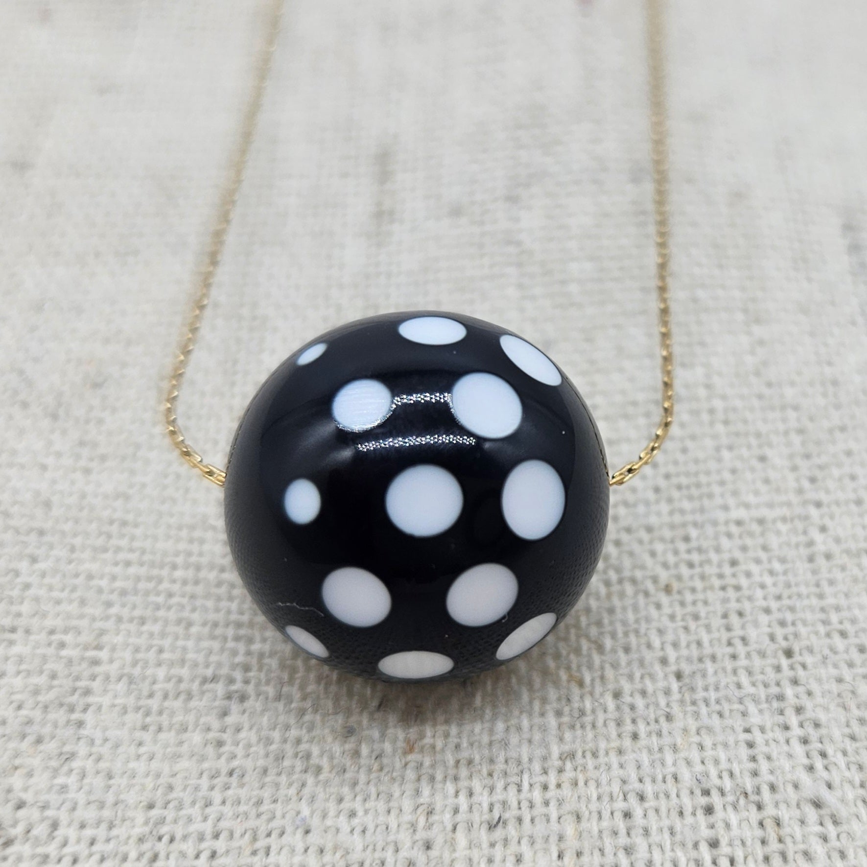 Black necklace with white polka dots on a textured beige background