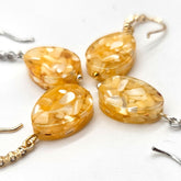 Four amber colored teardrop earrings taken at an angle laying on a white surface