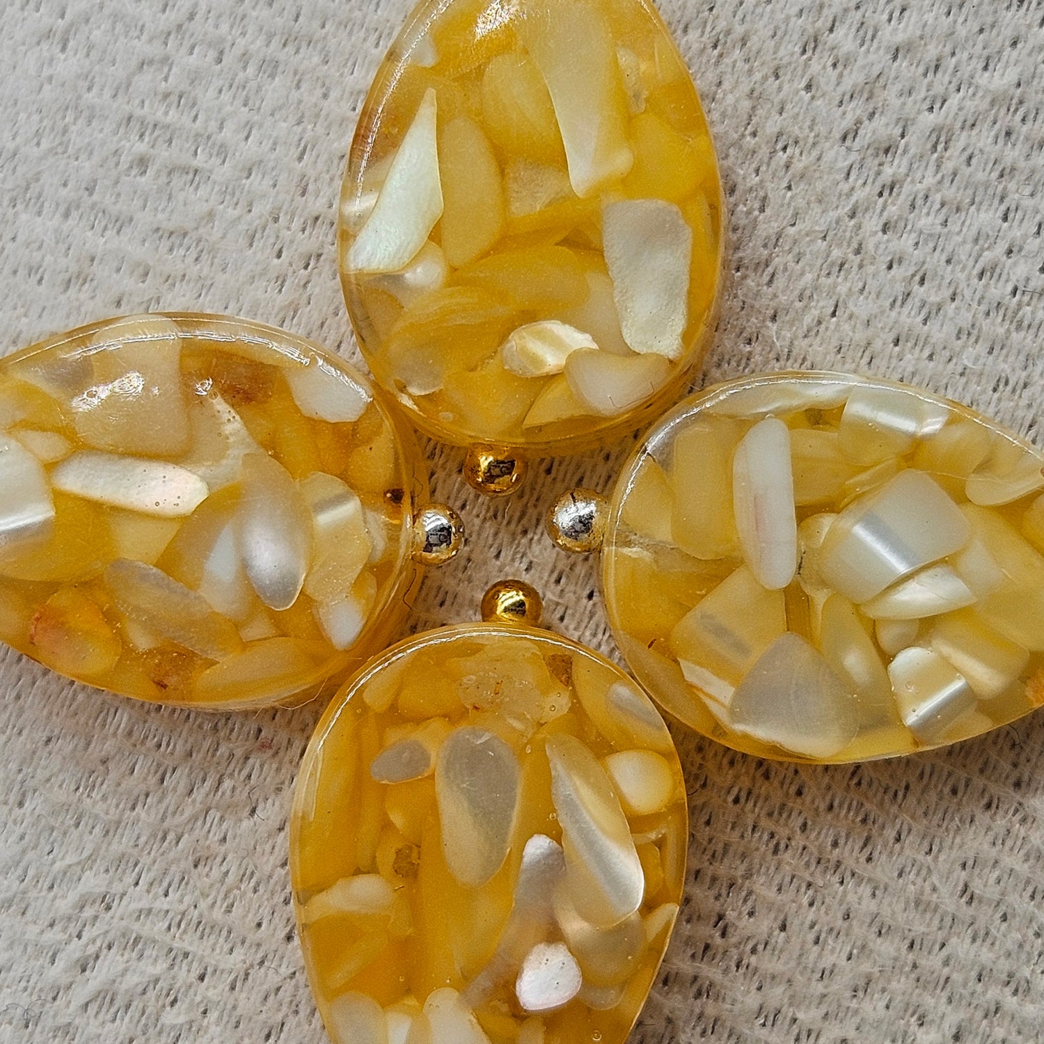 Four yellow and white marbled earrings with gold and silver accents on a textured surface.