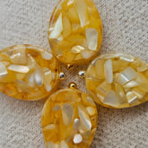 Four yellow and white marbled earrings with gold and silver accents on a textured surface.