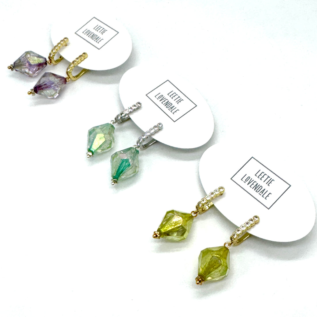 Set of earrings with green and purple gemstones on white cards with &