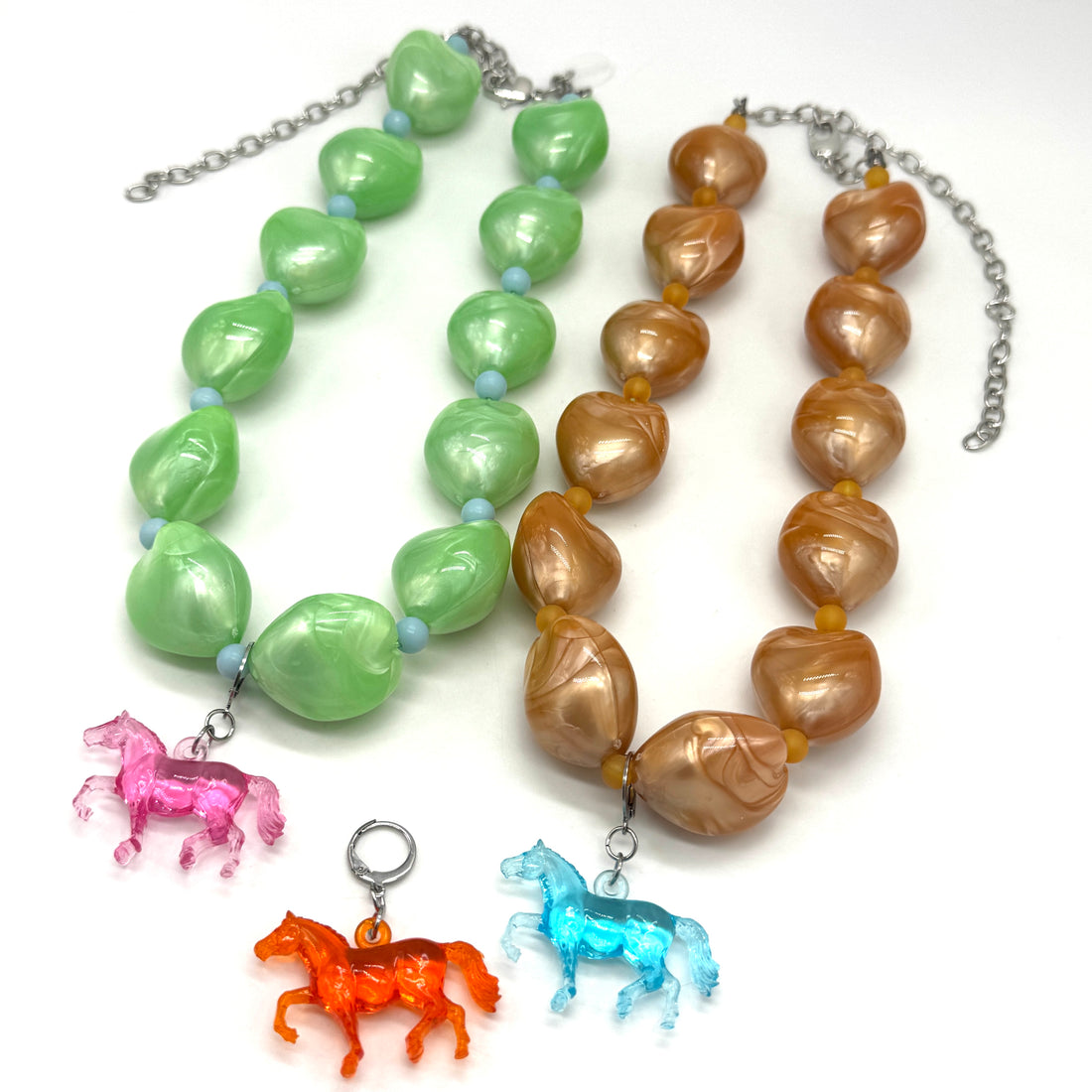 Two necklaces with green and brown beads and horse charms on a white background