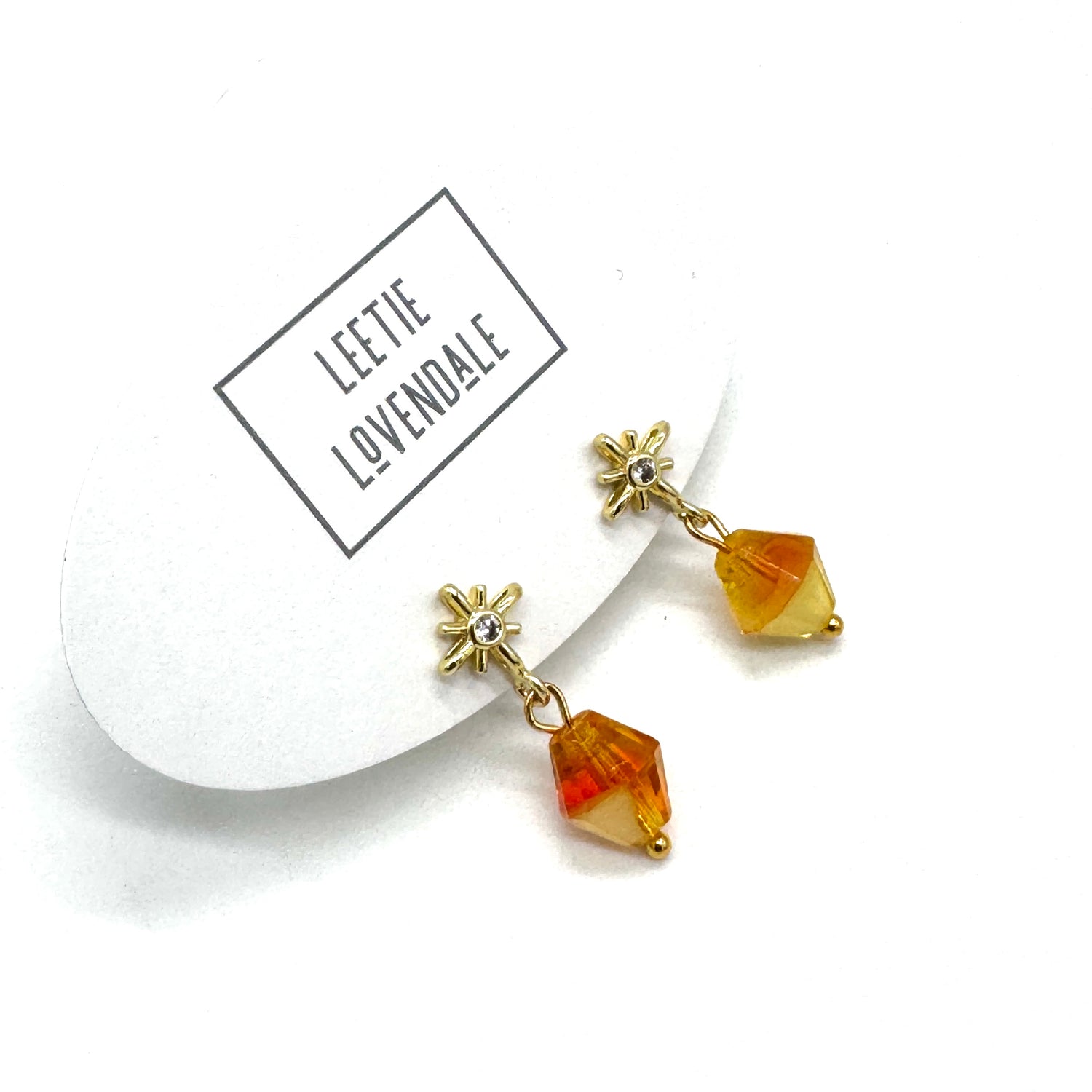 Pair of gold and amber crystal earrings on a white background with &