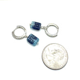Pair of silver hoop earrings with blue gemstones next to a quarter for scale on a white background