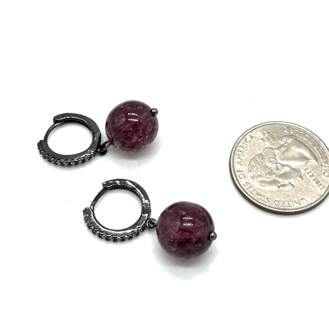 Pair of small hoop earrings with purple beads next to a quarter for scale on a white background
