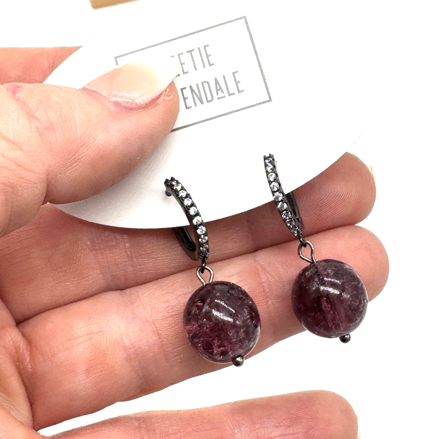 Purple gemstone earrings held in a hand with a &