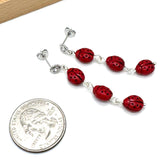 Red beaded earrings next to a U.S. quarter for size comparison on a white background