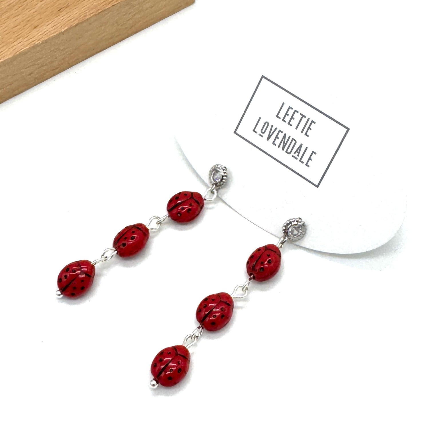 Necklace with red beads and silver clasps on a white background, featuring the brand &