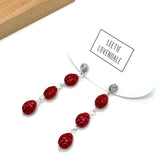Necklace with red beads and silver clasps on a white background, featuring the brand &